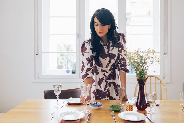 a happy elegant woman standing and preparing table for lunch before guests come