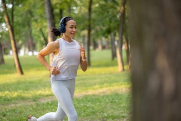 happy female athlete listening music while jogging in spring day at the park