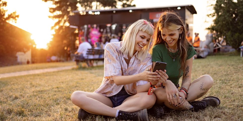 happy female festival goers using smart phone at sunset