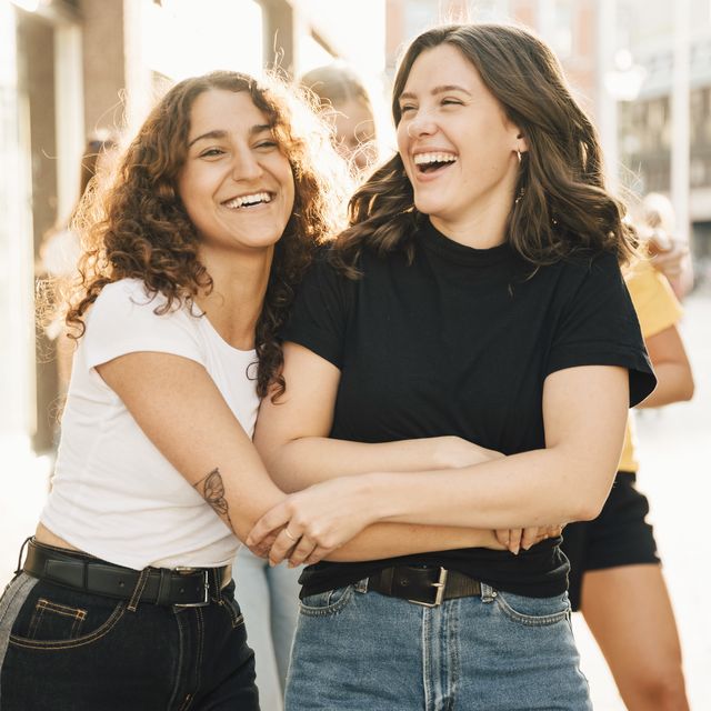 Happy female friends embracing in city during sunny day
