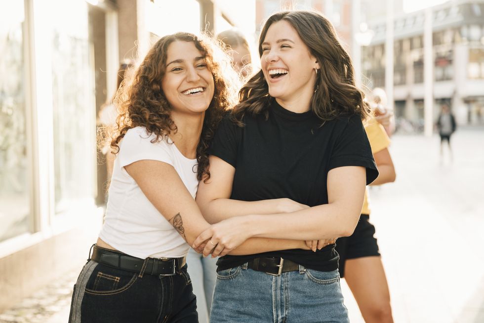 Happy female friends embracing in city during sunny day