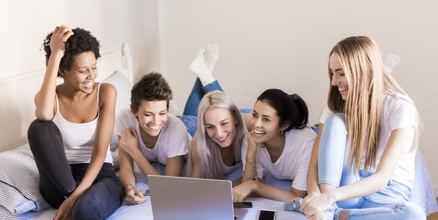 Happy female friends using laptop in bedroom