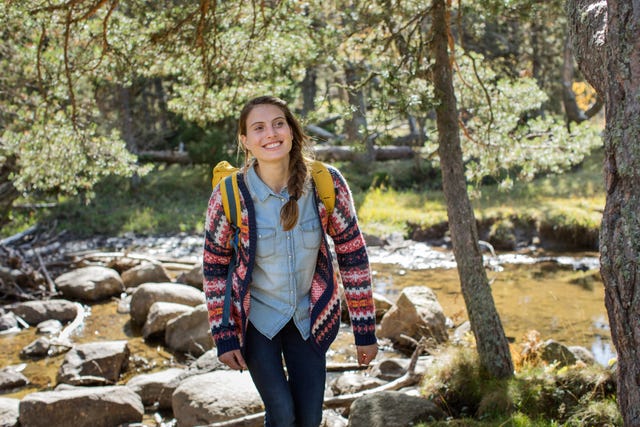 una mujer sonriente camina por un bosque cerca de un rio