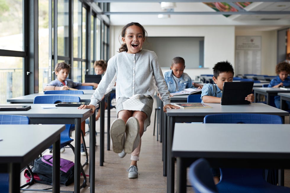 happy girl balancing between tables with feet in the air in classroom