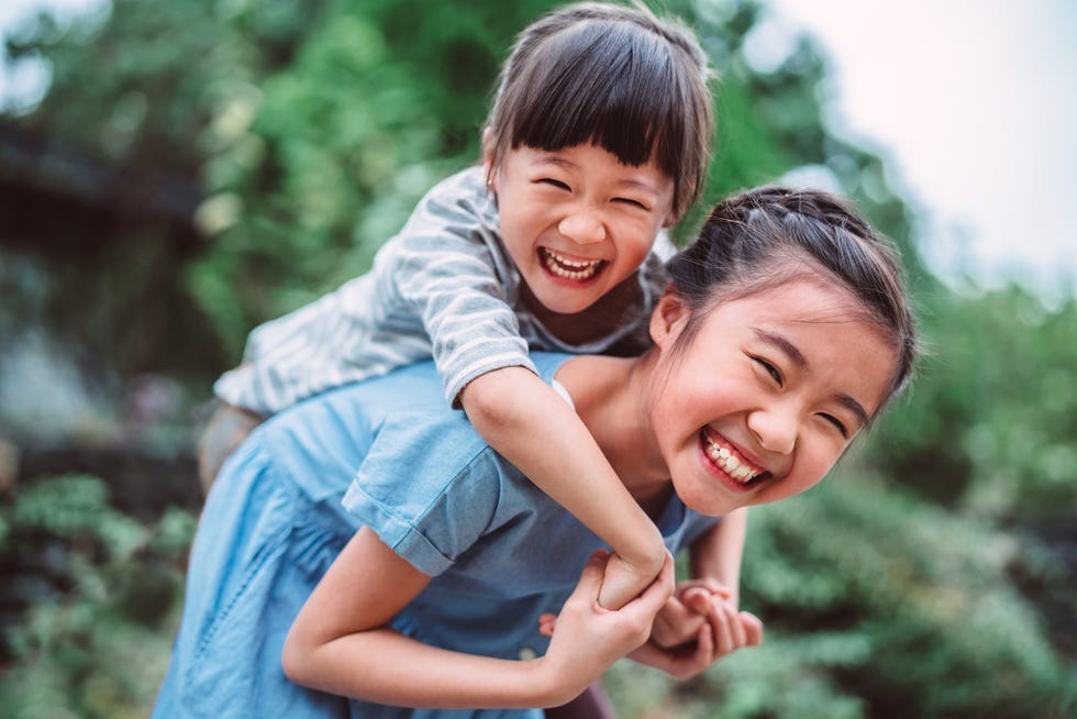 girl carrying her little sister on back in park joyfully