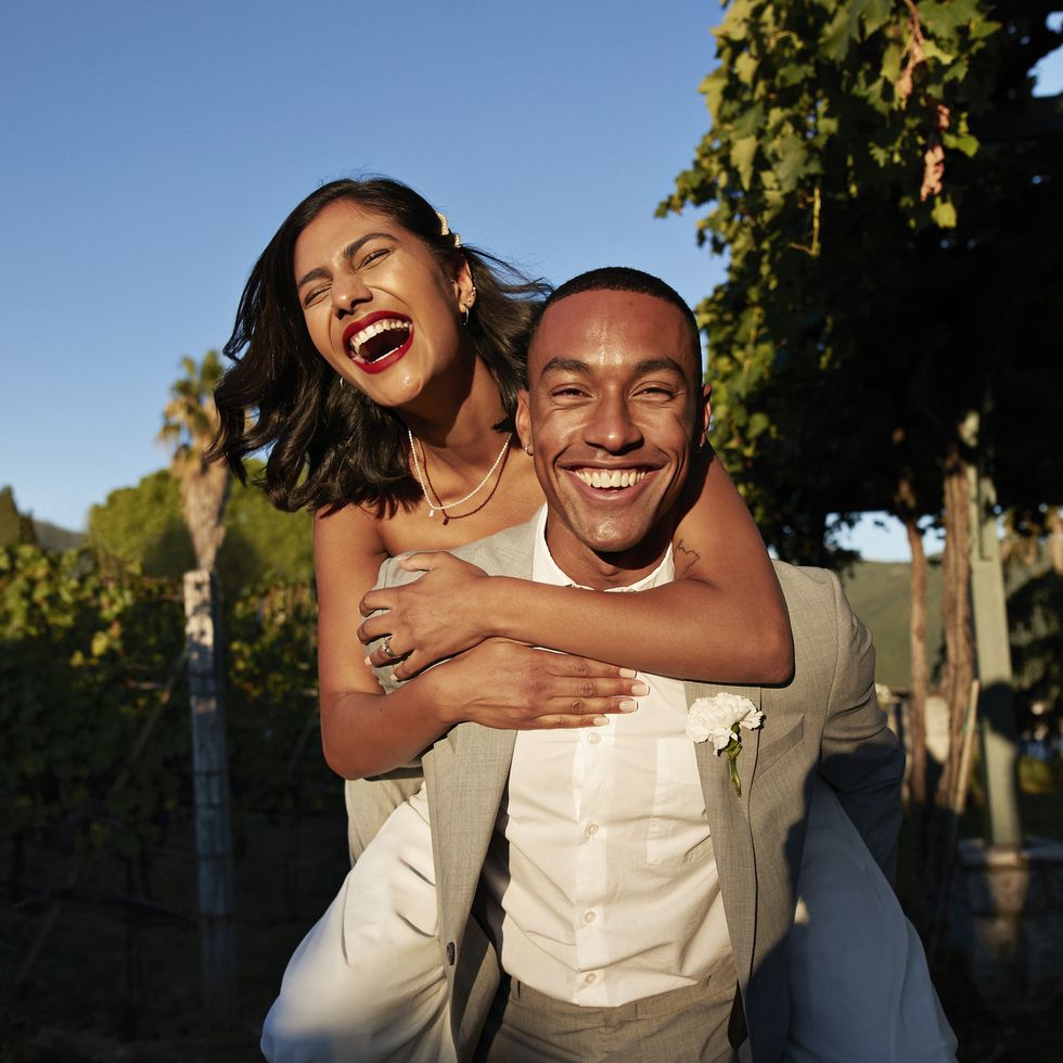 happy groom piggybacking bride in vineyard