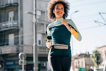 happy health conscious african american woman running in the city streets