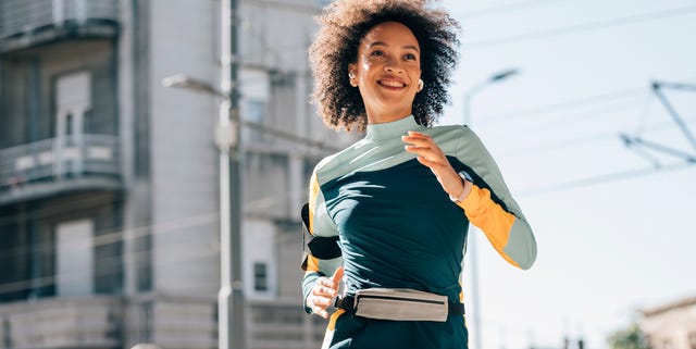 happy health conscious african american woman running in the city streets