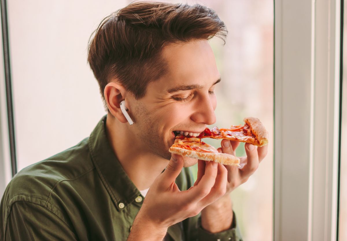 happy hipster man eating tasty slice of italian pizza during lunch break