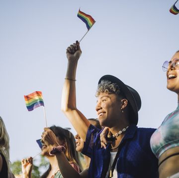 happy man and woman with hands raised holding rainbow flags while enjoying in gay pride parade