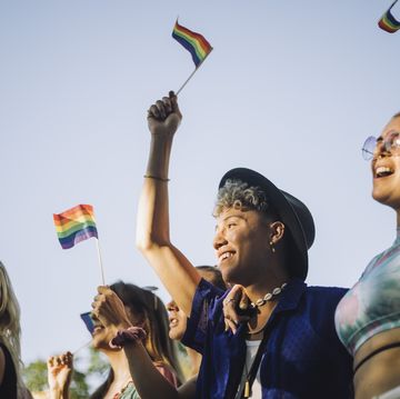 happy man and woman with hands raised holding rainbow flags while enjoying in gay pride parade