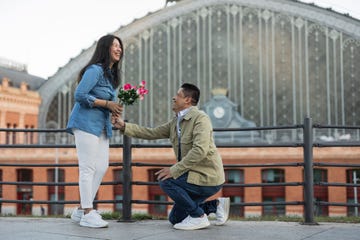 happy man giving flowers to woman and proposing at footpath on valentine's day