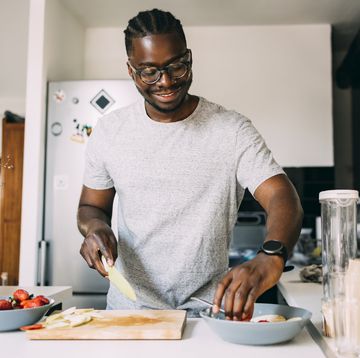 a happy man with glasses preparing healthy breakfast while standing in the kitchen