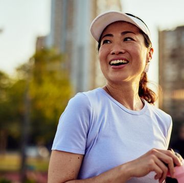 happy mature asian woman drinking water after exercising in the city