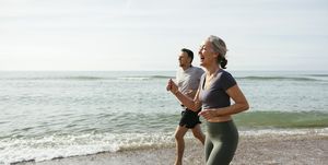 happy mature couple laughing and running in water at beach