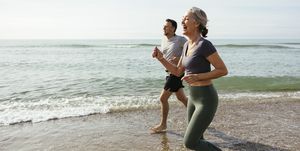 happy mature couple laughing and running in water at beach