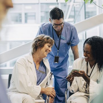happy mature female doctor sharing smart phone with coworkers during coffee break