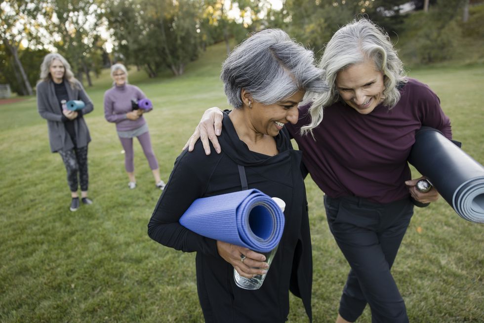 happy mature women friends walking with yoga mats in park