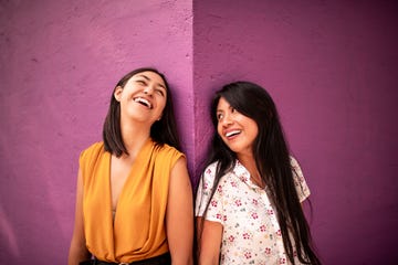 two girls look at each other and laugh against a purple wall