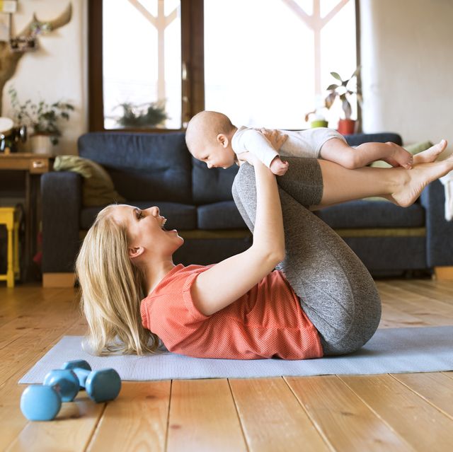 happy mother lifting up baby at home lying on mat