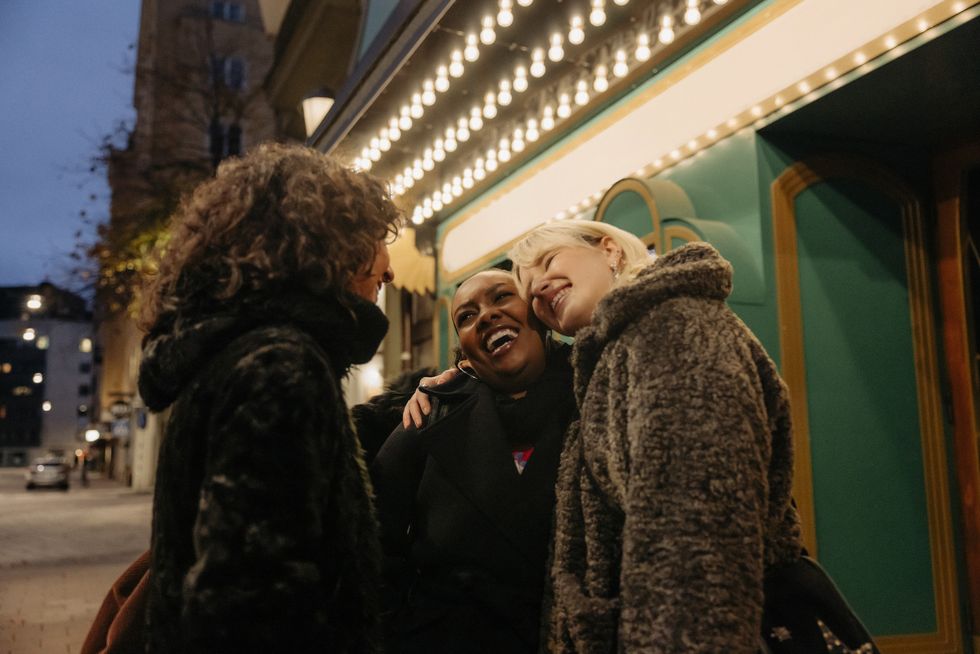 happy multiracial female friends greeting outside movie theater at night