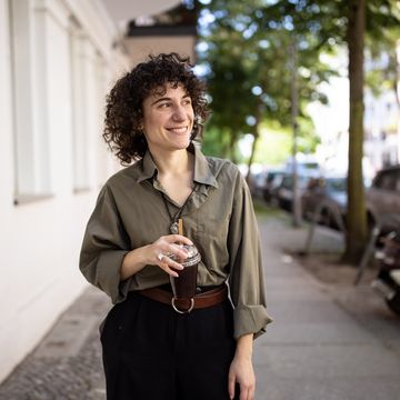 happy non binary person walking outside with a coffee cup