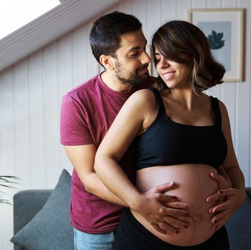 happy pregnant couple hugging and holding the baby belly while enjoying pregnancy together at home