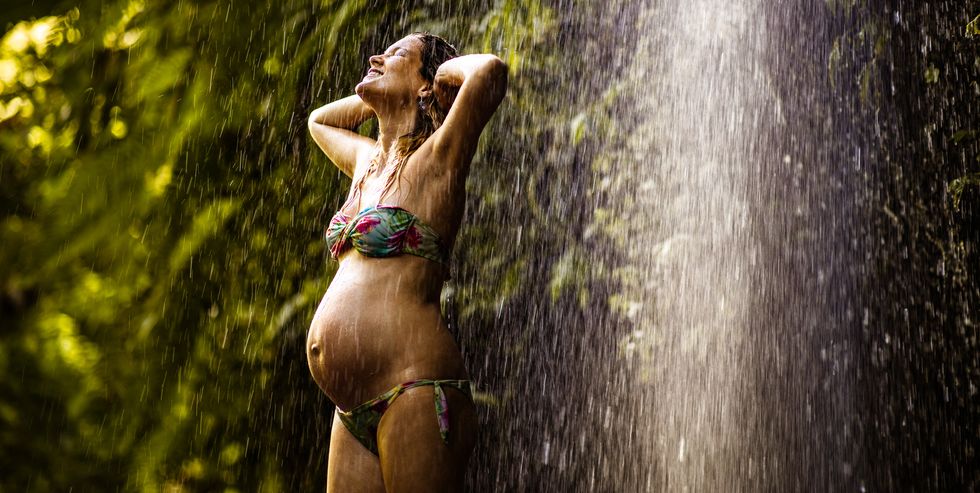 Happy pregnant woman enjoying under the waterfall in nature.