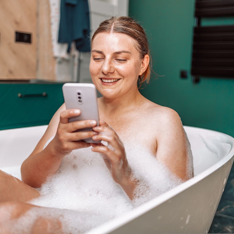 happy pretty caucasian woman using mobile phone while having a bath at home