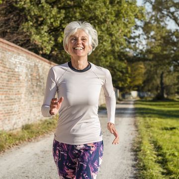 happy senior woman running along brick wall in a park