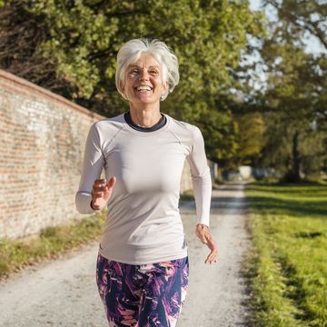 happy senior woman running along brick wall in a park