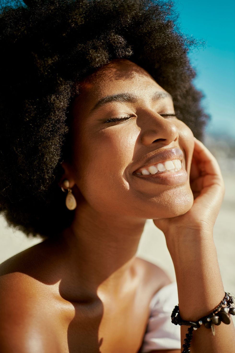happy, smiling and beautiful woman with an afro closed eyes closeup attractive and stylish young black female wearing makeup with good skin looking stunning enjoying the sun on a summer day