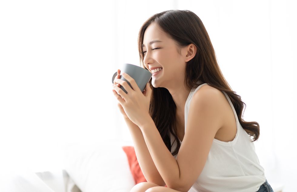 happy smiling beautiful asian woman awaking with cup of coffee at bedroom with eyes closed people lifestyle concept