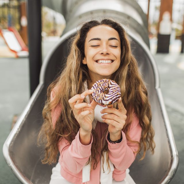 happy smiling young woman enjoying chocolate donut on children playground tasty and sweet fast food