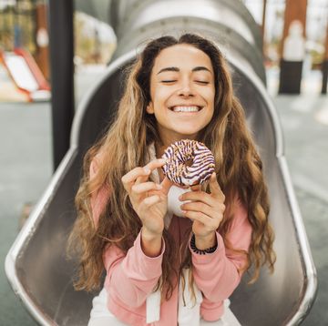 happy smiling young woman enjoying chocolate donut on children playground tasty and sweet fast food
