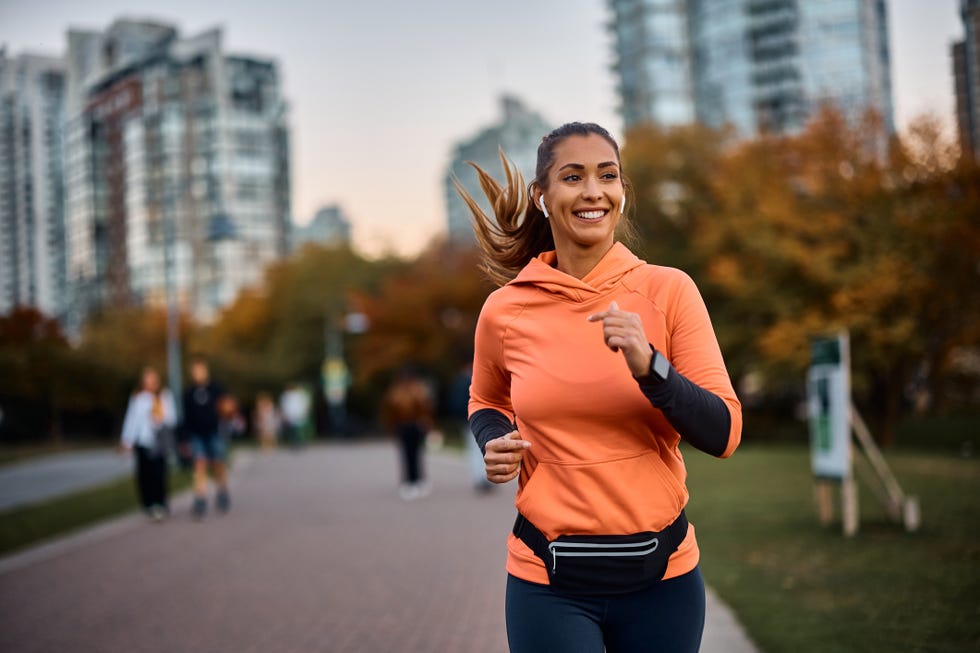 happy sportswoman with earbuds running in the park