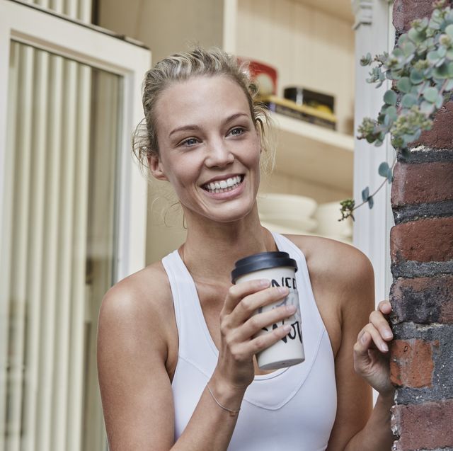 happy sporty young woman with takeaway drink at house entrance