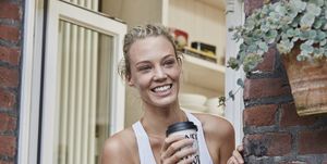 happy sporty young woman with takeaway drink at house entrance