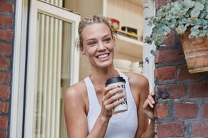 happy sporty young woman with takeaway drink at house entrance