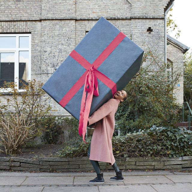 happy woman carrying large gift box on footpath