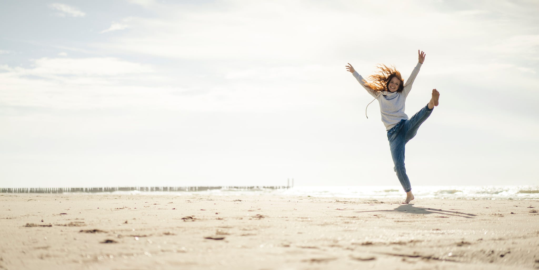 Happy woman having fun at the beach, dancing in the sand