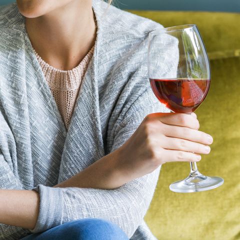 Happy woman holding glass of red wine on sofa