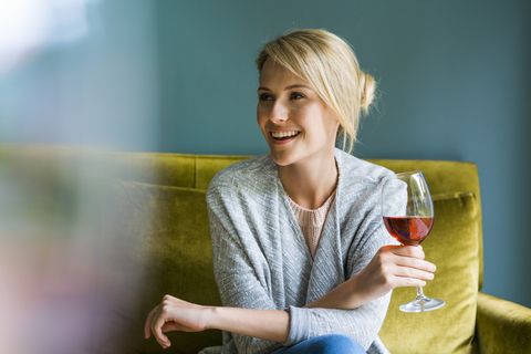 Happy woman holding glass of red wine on sofa
