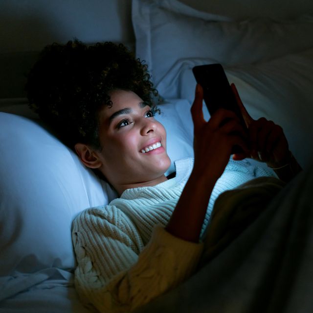 happy woman in bed texting on her cell phone