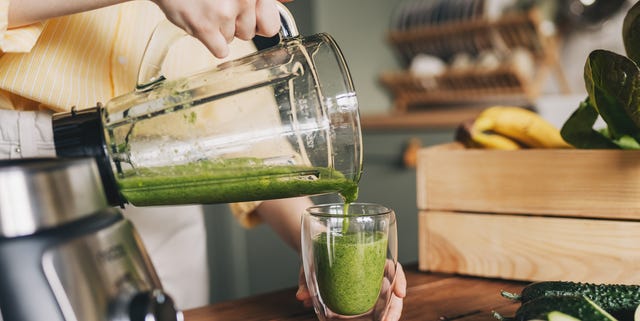 Happy woman on detox diet, pouring green cocktail from mixer into glass in kitchen happy woman on detox diet, pouring green cocktail from mixer into glass in kitchen