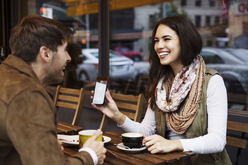 happy woman showing mobile phone to boyfriend while enjoying coffee at cafe