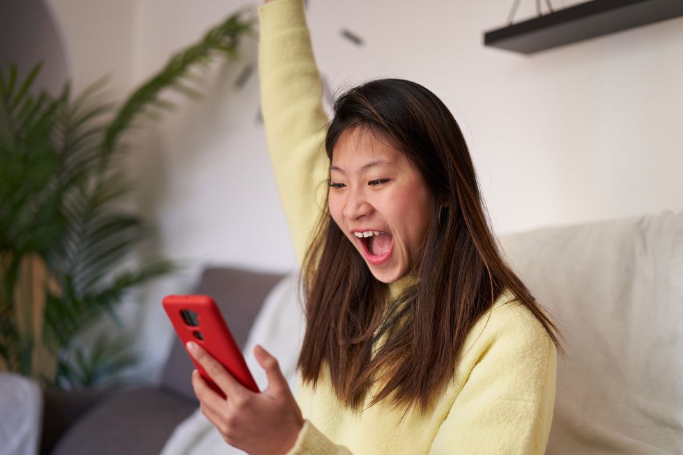 happy woman wining the lottery sitting at home using phone