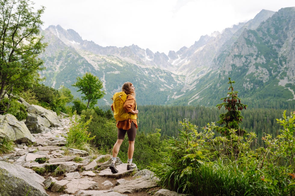 happy woman with a yellow hiking backpack enjoying the mountain landscape