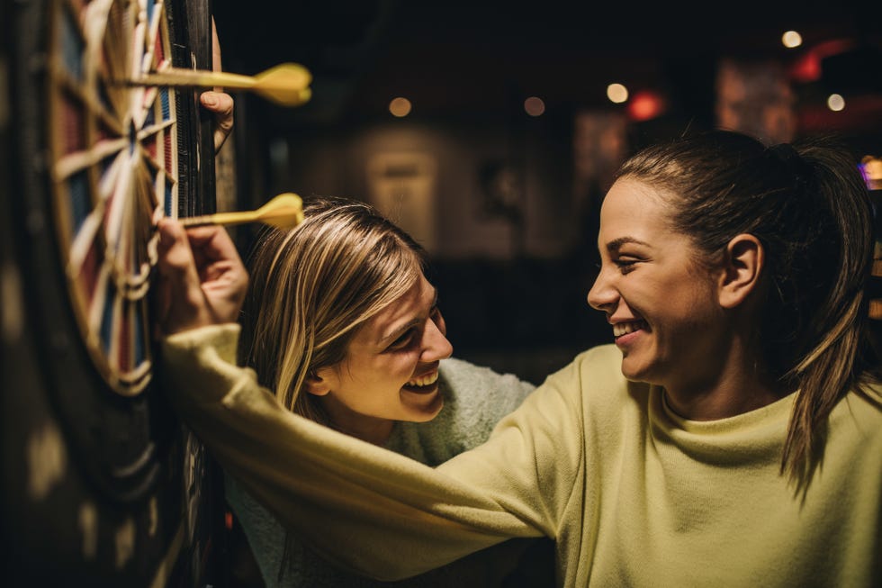 Happy women talking while removing darts from dartboard.