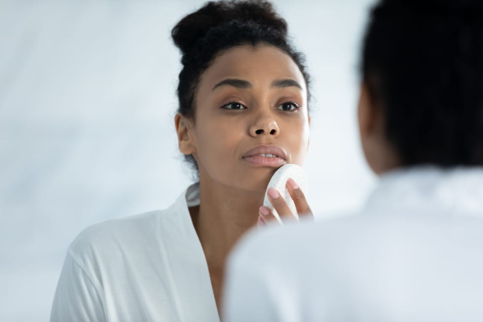 happy young african woman exfoliating face with sponge